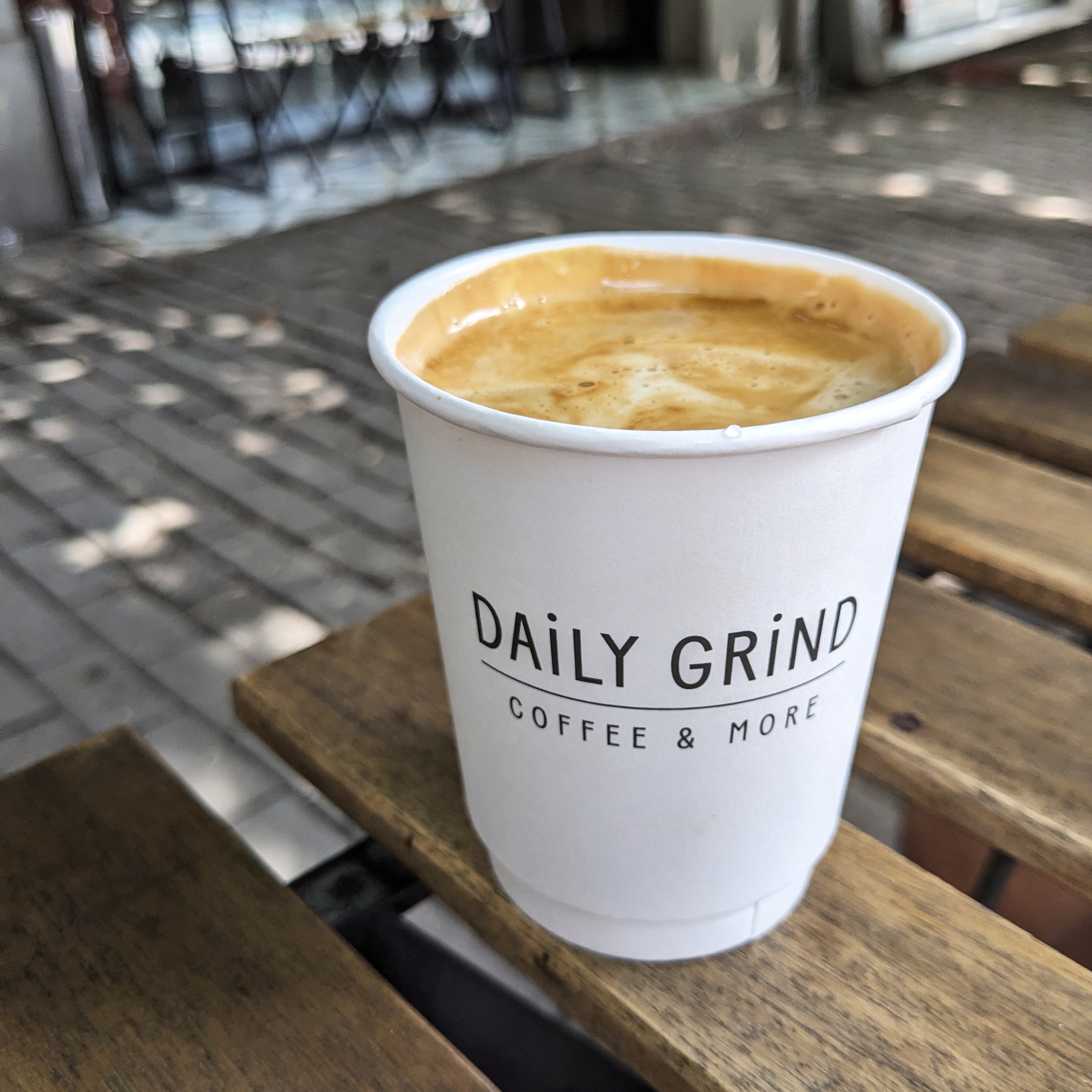 A flat white in a paper cup on a wooden table outside Daily Grind, one of the best cafes in Tbilisi