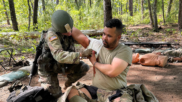 Army 2nd Lt. Olivia Agee, left, in a forest setting, assisting a man with an "arm wound" during a field exercise scenario.