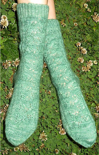 Someone wearing a pair of green socks. They have a lace leaf pattern along the leg and top of the foot.