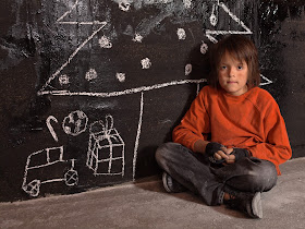 PIc of poor homeless boy at Christmas sitting on ground with chalked Christmas tree and presents