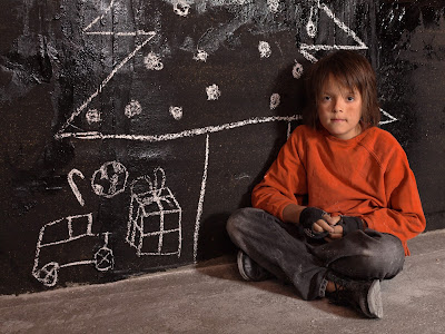 PIc of poor homeless boy at Christmas sitting on ground with chalked Christmas tree and presents