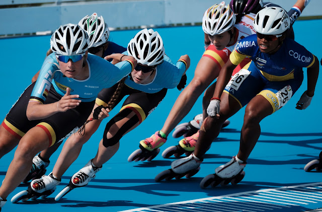 Speed skaters circle around the rink in a tight group.