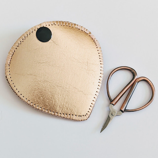 Paper fabric scissor holder, with decorative stitching around the edge and a snap closure, and a pair of embroidery scissors