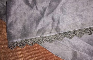 A photo of shiny black linen voile folded artistically, with narrow scalloped lace sewn along one edge.