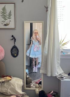 The author is wearing a gingham dress and converse shows with large ribbons for laces. They have on a big pair of glasses and a long wig with bangs.