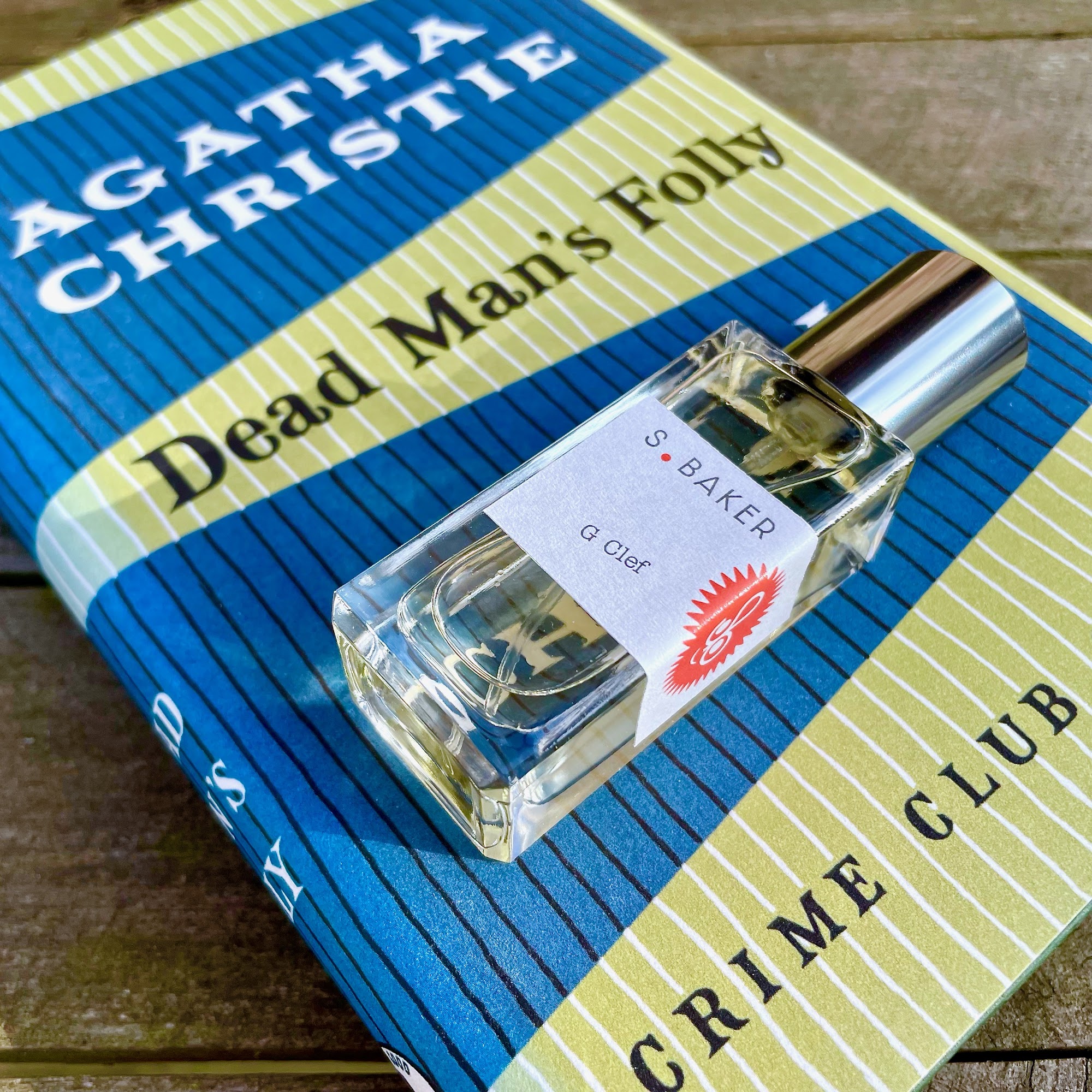 A bottle of G clef perfume on top of a copy of Agatha Christie's Dead Man's Folly book
