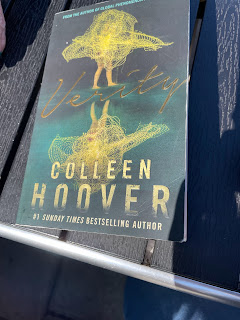 The front cover of Verity by Colleen Hoover. It's green and gold, with the wispy illustration of a girl standing on a wall. Across the bottom it says, 'from the sunday times best selling author.'