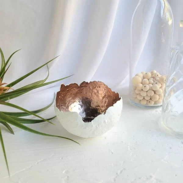 handmade white paper pulp bowl with rose gold painted interior displayed with green plant and jar containing unpainted wooden beads