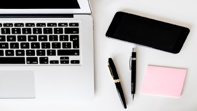 Digital Marketing work station with a computer, mobile phone, notepad and two pens.