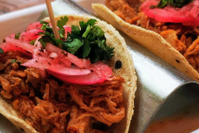 A Close up image of the Gluten Free Pork Pibil Tacos available at Wahaca, Southbank, the image shows juicy shredded pork, pink pickled onions and is topped with fresh coriander.