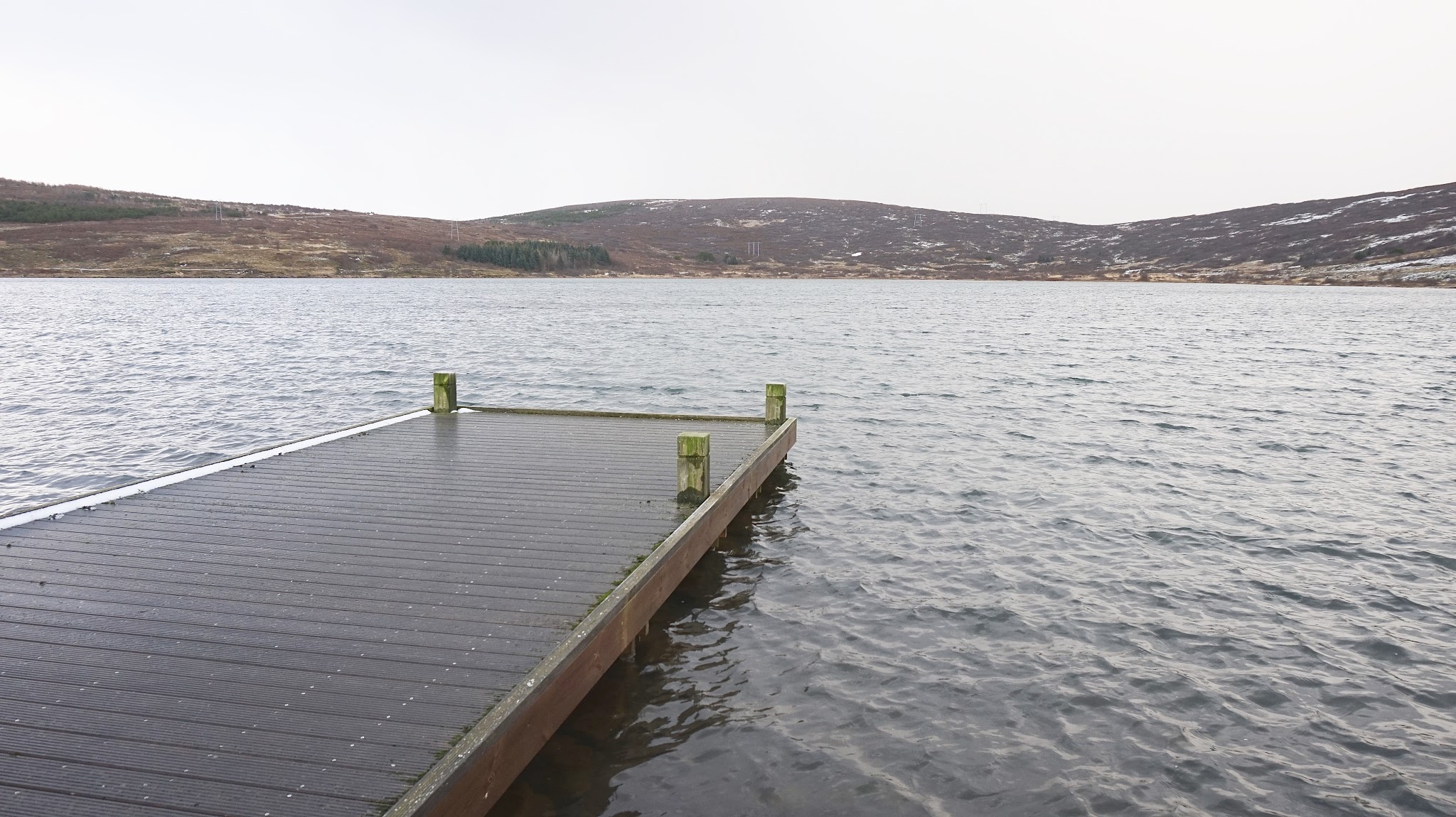 wooden jetty overlooking huge lake, snowy hills in the background