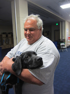 Coach Dom is holding Coach.  Coach (the dog) is staring into the camera.