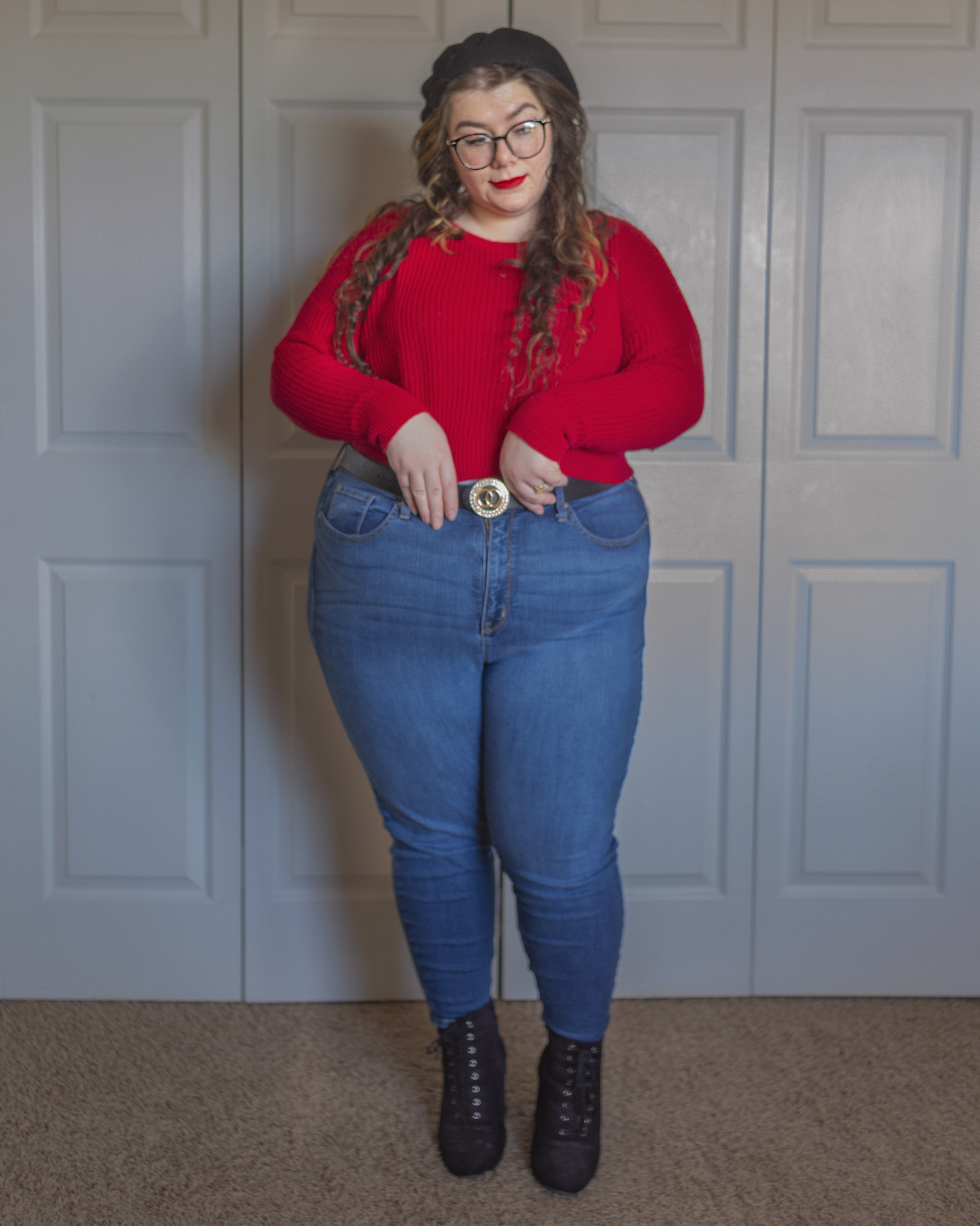 An outfit consisting of a black wool beret, a red cropped sweater over high waist medium wash blue skinny jeans and black lace up booties.