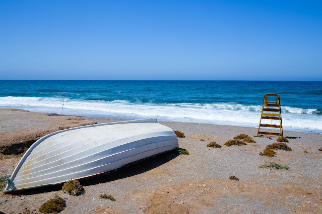 Una barca y un puesto de vigía sobre la arena de la playa con las azules aguas del mar al fondo