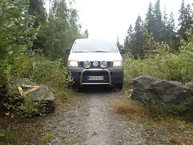 Soratien molemmin puolin kaksi lohkaretta ja niiden takana odottaa auto, joka on leveämpi kuin lohkareiden väliin jäävä tie