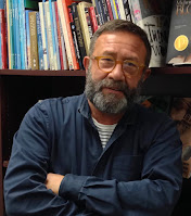 A photo of Neal Porter, standing with arms folded in front of a bookshelf