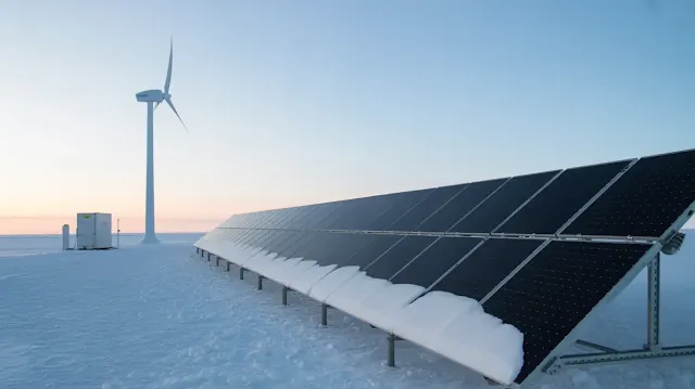 A photograph showcasing a row of sleek, modern solar panels installed on a research station in Antarctica. The panels are covered in a thin layer of snow, but still actively generating power, contrasting against the stark white landscape and reflecting the pale blue sky. In the background, a single, gracefully curved wind turbine spins silently, harnessing the fierce Antarctic winds, while a hybrid system connecting both sits nearby, all contributing to "Clean Energy for the Poles". The scene is bathed in a soft, diffused light, emphasizing the quiet resilience of sustainable technology in an extreme environment.