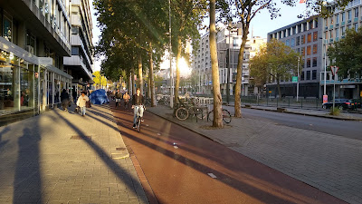 Une large rue bordée de commerces avec des appartements au-dessus, des trottoirs et des pistes cyclables de part et d'autre.