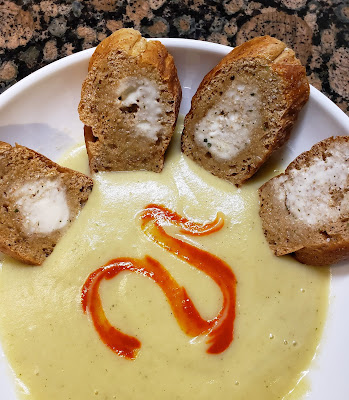 a bowl of cauli-potato soup wtih garlic toast and a swirl of hot sauce