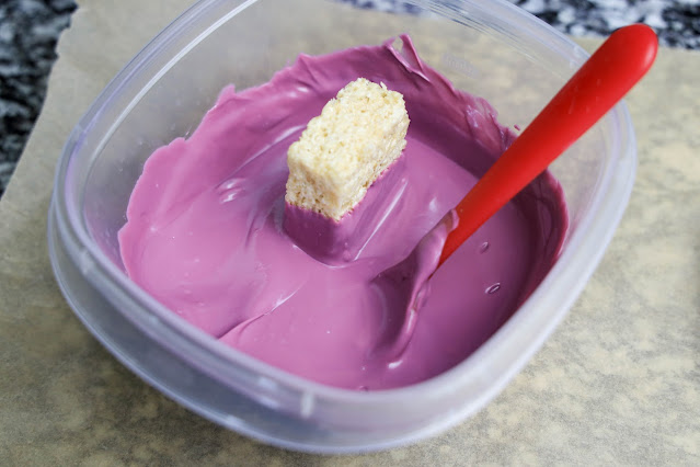 krispie treat being dipped into purple candy melts.