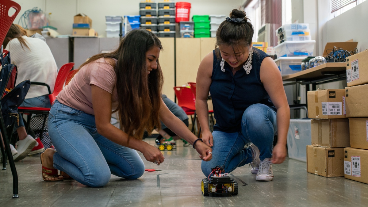 Two teachers experiment with a small robot during a coding workshop.