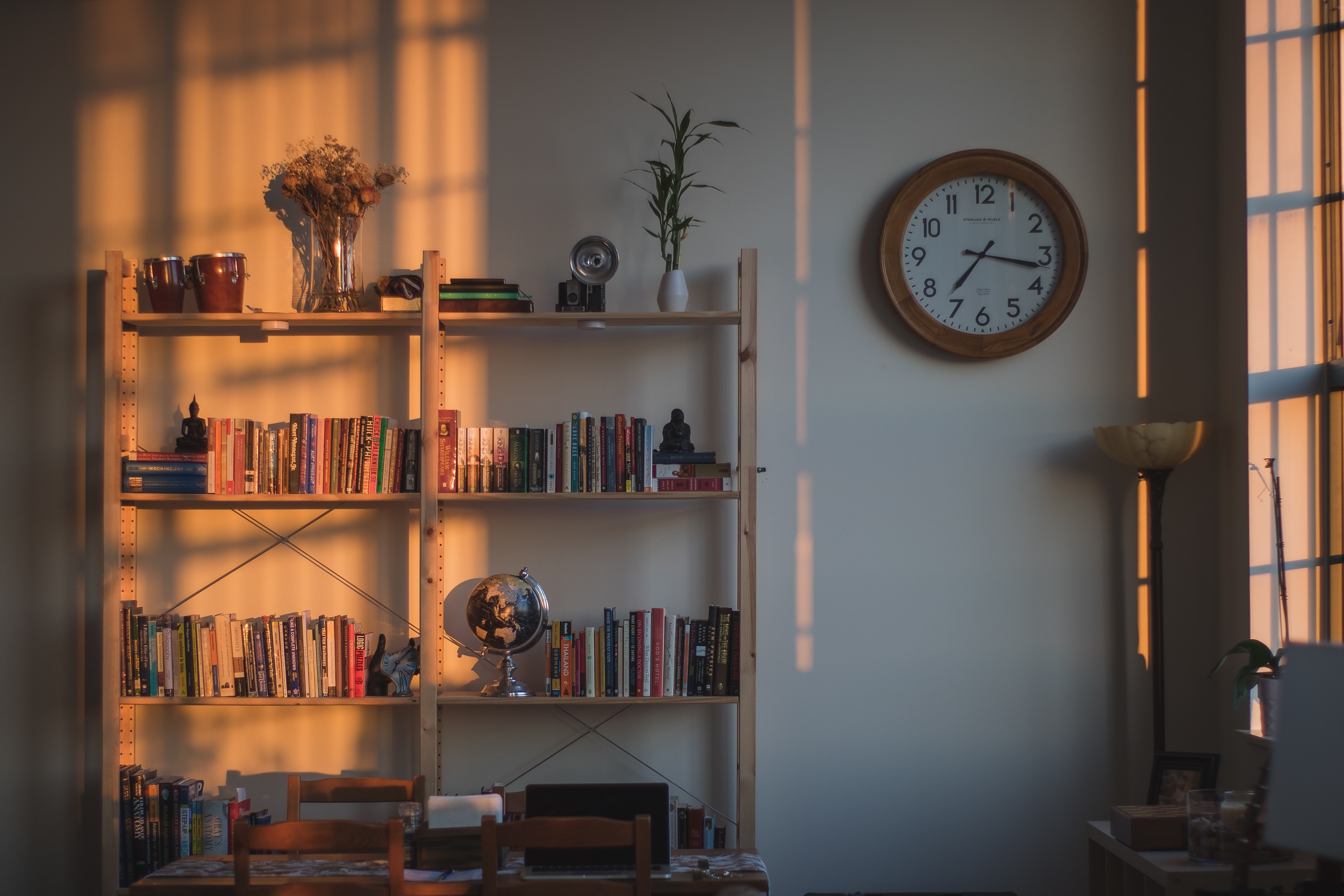 an open wooden bookcase filled with books plus decorative items. there is light streaming through a window casting beautiful shadows