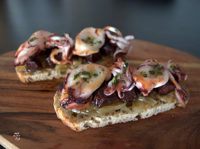 Una tapa gastronómica: base de pan tostado, cebolla caramelizada, dados de butifarra negra salteada y chipirones con su ajo y perejil