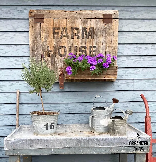 Photo of a potting bench with lavender topiary and watering cans, farmhouse sign/planter