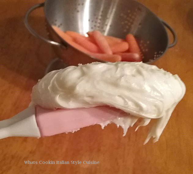 This is a photo of whipped cream cheese frosting for a carrot cake that is made from a cake mix. There are carrots in a colander in the backround.