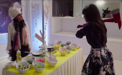 Kamilah looks calmly across the omelet bar at Tahani, who is wielding a bright red axe