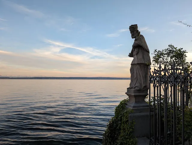 Sculpture of a king in the foreground and the sunset over Lake Constance in the Background