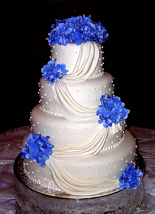 Four tier white wedding cake with draping edible pearls and blue hydrangeas