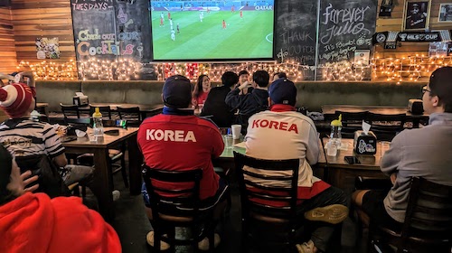 Two men in Korea jackets watch the match