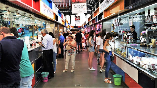 Calle del mercado llena de gente comprando en los puestos.