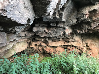 A view inside the cave showing the ground covered in nettles and the red rock of the cave rising up and around.  Photograph by Kevin Nosferatu for the Skulferatu Project.