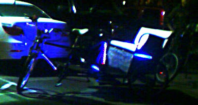 Pedicab with multiple banks of LED lights.  The lights are blue and pink.  The seat of the Pedicab is white.