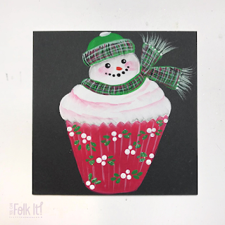 Handpainted snowman topped cupcake design Christmas card. Thesnowman wears a green tartan hat and scarf and the red cupcake wrapper is decorated with white berries and leaves 