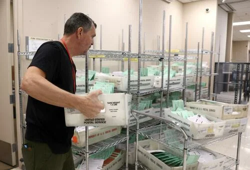 An election worker carries trays filled with mail in ballots to open and verify at the Maricopa County Tabulation and Election Center in Phoenix, Ariz., on Nov. 11, 2022