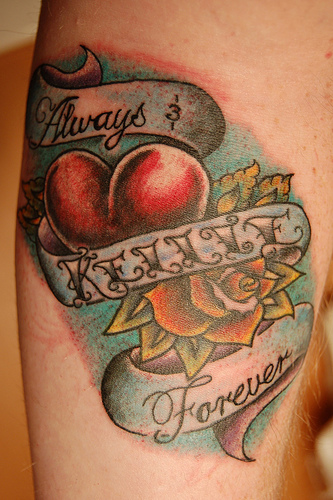 A mans arm with having a tattoo of a heart and a rose surrounded by a banner