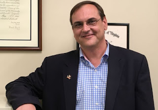 A man in a navy blazer and blue and white gingham shirt