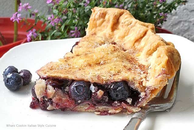 this is a sliced of homemade blueberry pie on a white plate