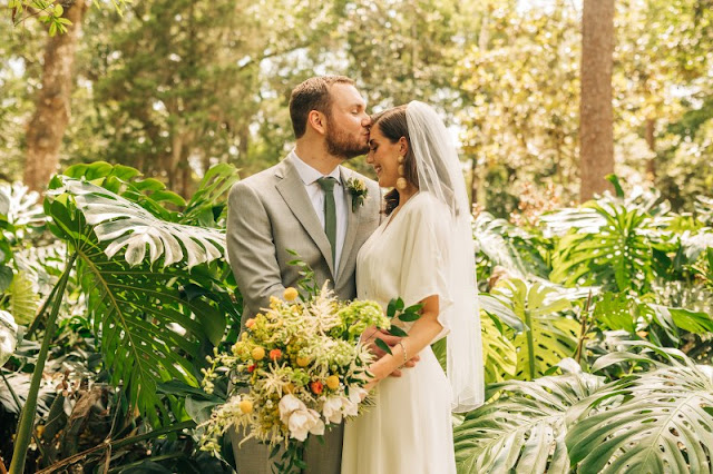 groom kissing bride on forehead in front of forest