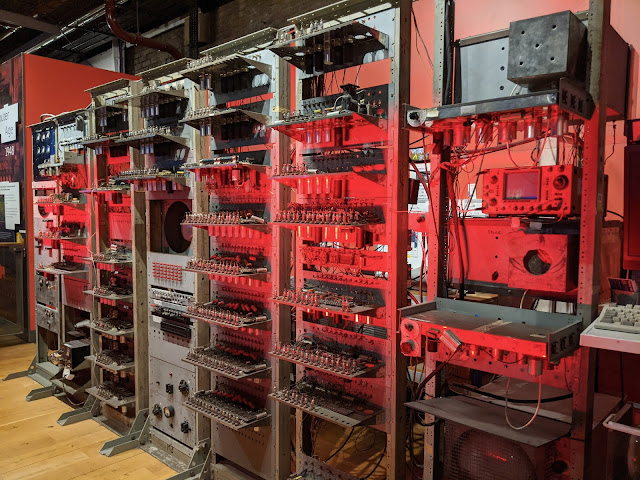 Old computer in racks with valves and screens visible. Lit by red light