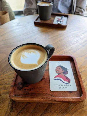 Cappucino on a wooden tray next to a card with a drawn portrait of a lady