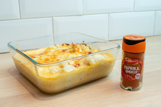 Cauliflower cheese cooked in a square glass dish and a bottle of Schwartz smoked paprika to the right.