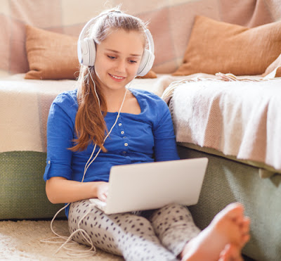 young girl sitting on the floor with a laptop and headphones on.
