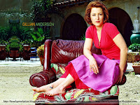 gillian anderson, sitting on reddish brown couch in red top and purple skirt with bare tattooed feet