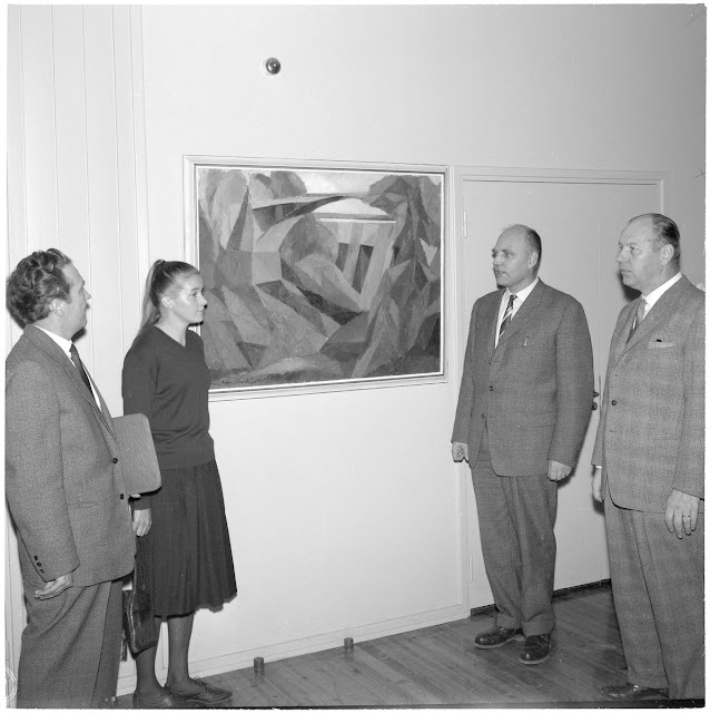 Henkilöitö seisoo molemmin puolin maalausta salissa. Abstrakti värimaalaus ei pääse oikeuksiinsa mustavalkokuvassa.