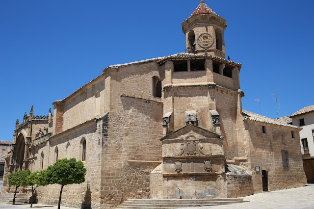 Antigua iglesia con una fuente y un campanario en la plaza de una ciudad.