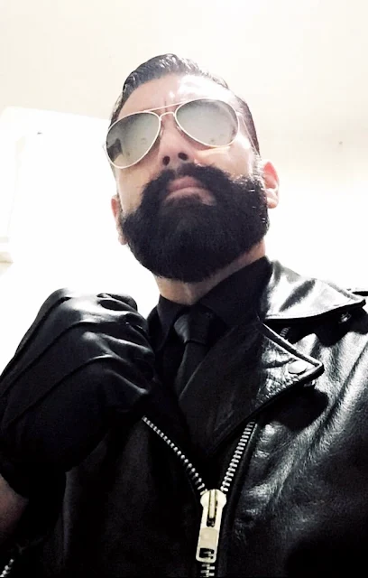 Bearded daddy with hair slicked back wearing shades with black leather jacket from chest upward making fist with tight gloves hand